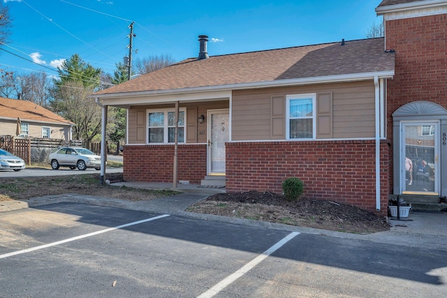 view of front of property with uncovered parking, brick siding, and a shingled roof