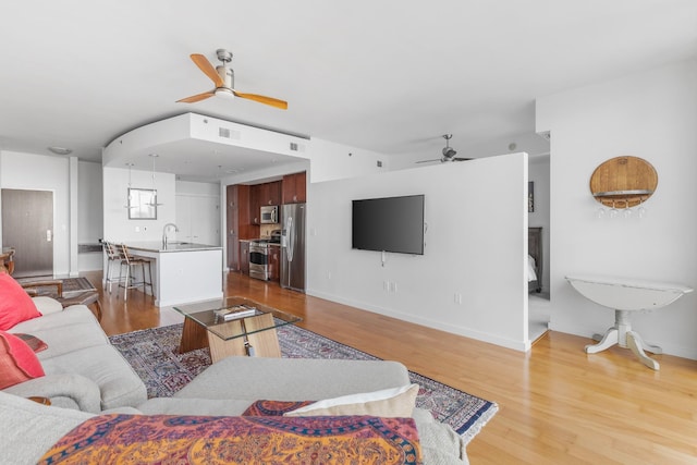 living area featuring visible vents, light wood-type flooring, a ceiling fan, and baseboards