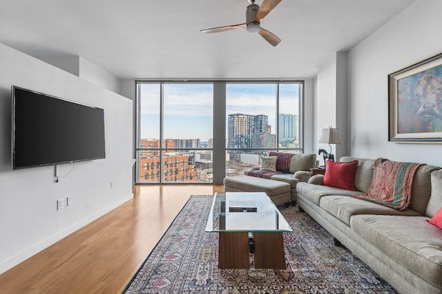 living room with expansive windows, wood finished floors, a ceiling fan, baseboards, and a view of city