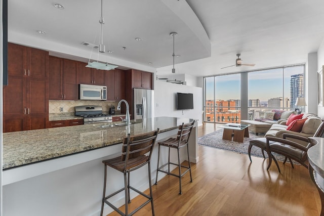 kitchen featuring stone counters, pendant lighting, stainless steel appliances, open floor plan, and a sink