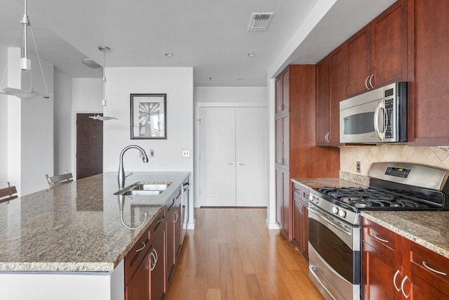 kitchen featuring light stone counters, decorative light fixtures, appliances with stainless steel finishes, a kitchen island with sink, and a sink