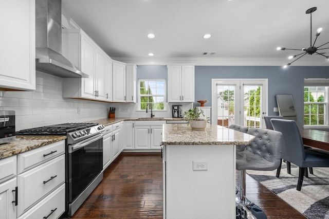 kitchen featuring a kitchen island, white cabinetry, light stone countertops, stainless steel gas stove, and wall chimney exhaust hood