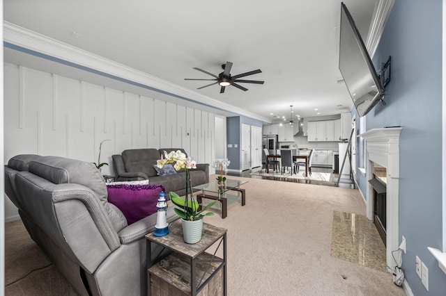 living area with light carpet, ceiling fan with notable chandelier, a fireplace, baseboards, and ornamental molding