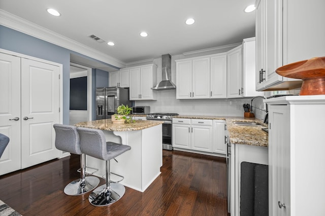 kitchen with white cabinets, wall chimney exhaust hood, a kitchen island, appliances with stainless steel finishes, and a sink