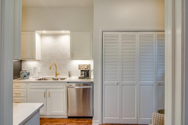 kitchen with a sink, white cabinetry, light countertops, stainless steel dishwasher, and backsplash