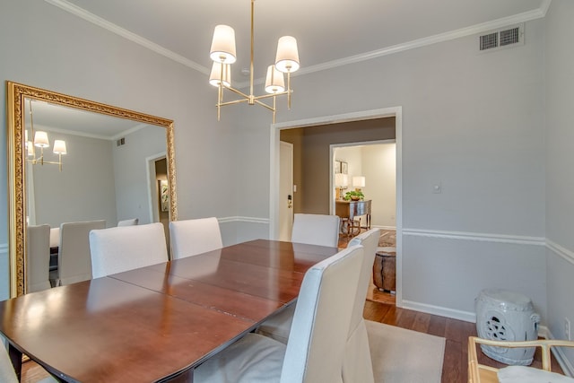 dining room featuring an inviting chandelier, crown molding, visible vents, and wood finished floors