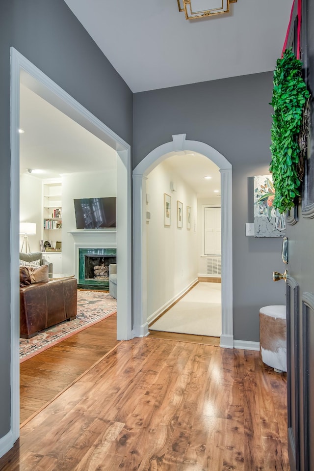 corridor with arched walkways, baseboards, wood finished floors, and built in features