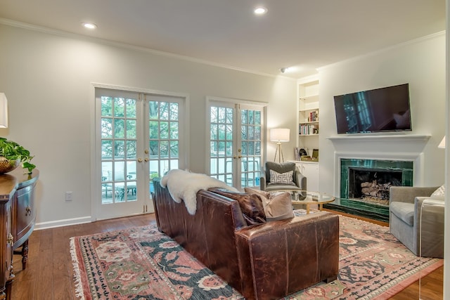 living room with a fireplace, wood finished floors, built in features, ornamental molding, and french doors