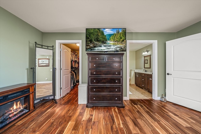 bedroom with connected bathroom, dark wood finished floors, a closet, a walk in closet, and a glass covered fireplace