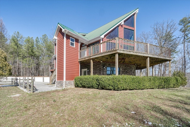 rear view of house with stone siding, a deck, metal roof, and a yard