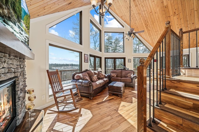 living area with a chandelier, stairs, a stone fireplace, light wood-type flooring, and high vaulted ceiling