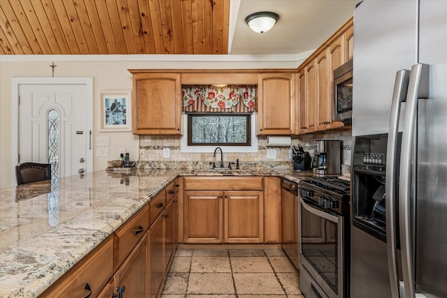 kitchen with light stone counters, stone tile floors, a sink, appliances with stainless steel finishes, and brown cabinetry