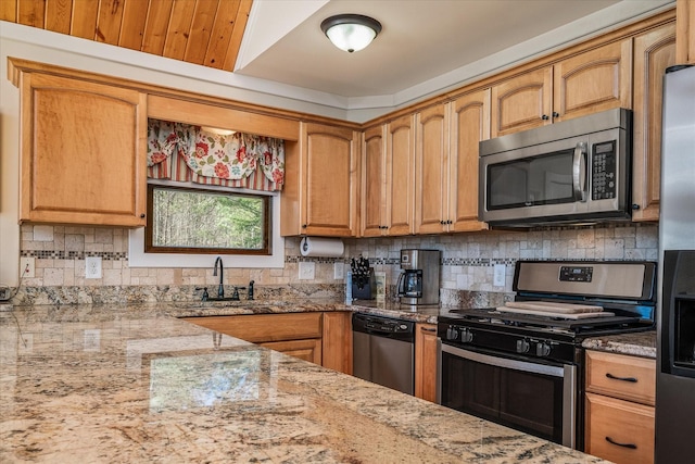 kitchen featuring decorative backsplash, brown cabinets, light stone countertops, stainless steel appliances, and a sink