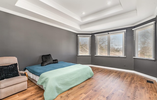 bedroom featuring a raised ceiling, multiple windows, crown molding, and hardwood / wood-style flooring