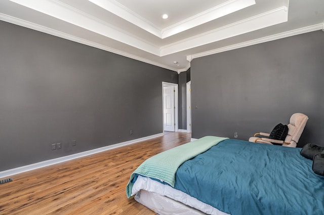 bedroom with recessed lighting, a raised ceiling, ornamental molding, wood finished floors, and baseboards