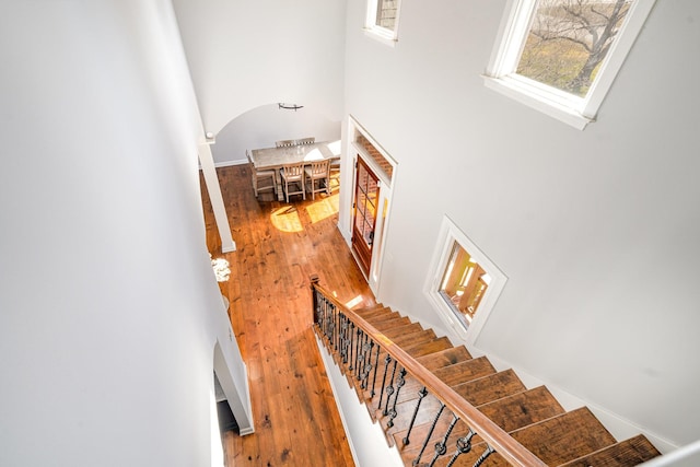 staircase with a high ceiling, arched walkways, and wood finished floors