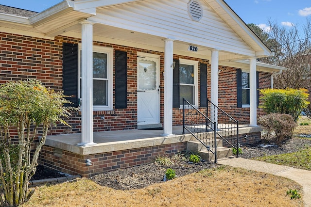 doorway to property featuring a porch and brick siding