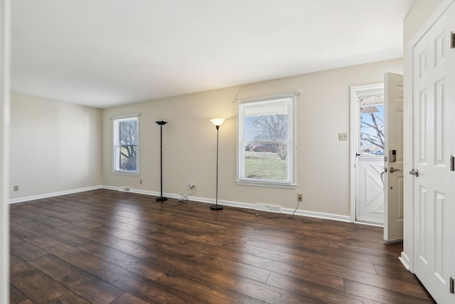 empty room with baseboards, visible vents, and dark wood-type flooring