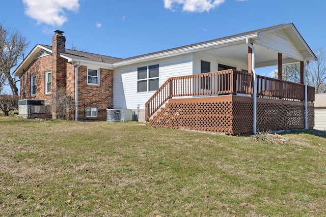 back of house with a deck, central AC, brick siding, a lawn, and a chimney