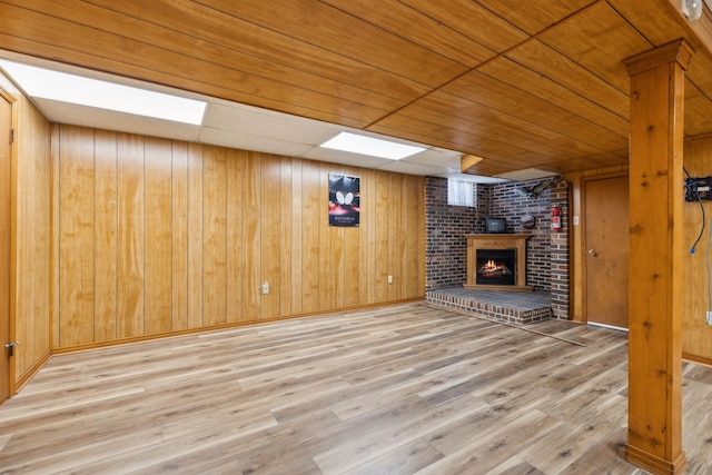 unfurnished living room with baseboards, a fireplace, light wood-style flooring, and wooden walls