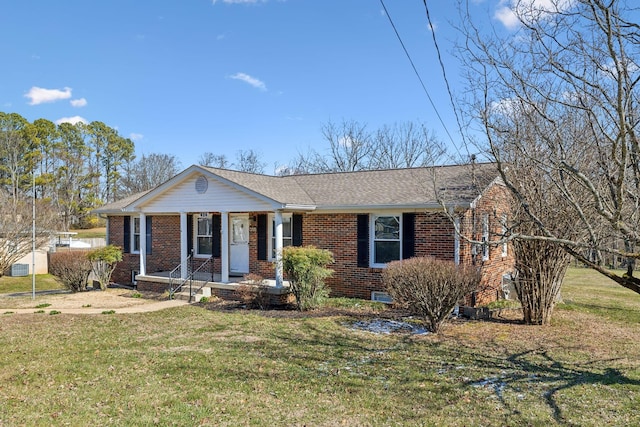 view of front of home featuring brick siding, a porch, a shingled roof, and a front yard