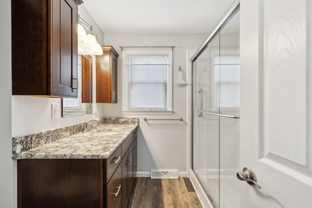 bathroom featuring wood finished floors, visible vents, vanity, baseboards, and a shower stall