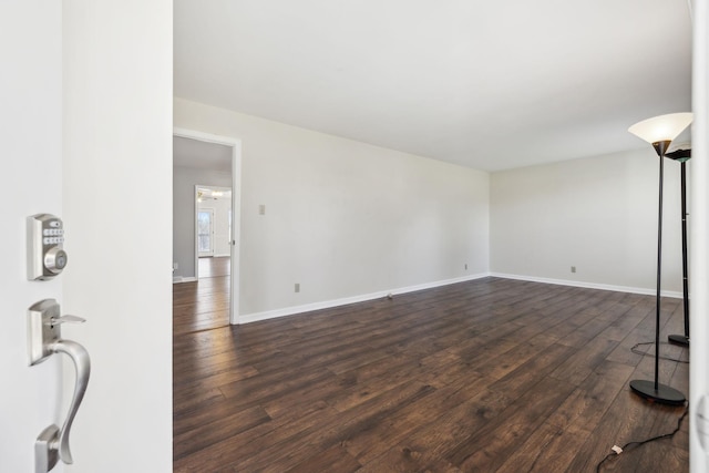 unfurnished living room with dark wood-type flooring and baseboards