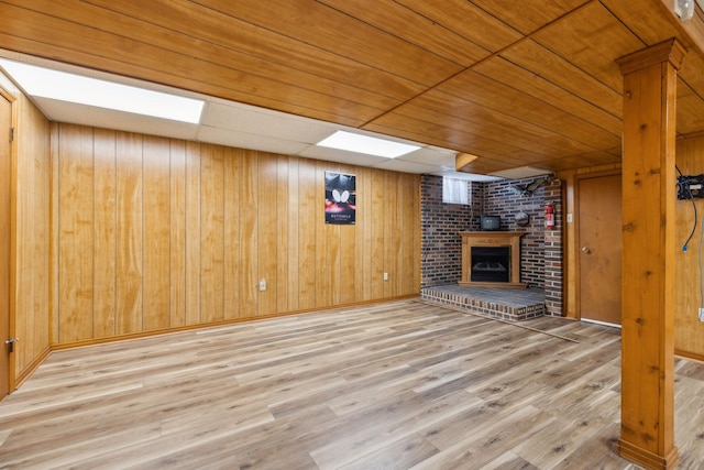 unfurnished living room featuring light wood finished floors, a brick fireplace, and wood walls