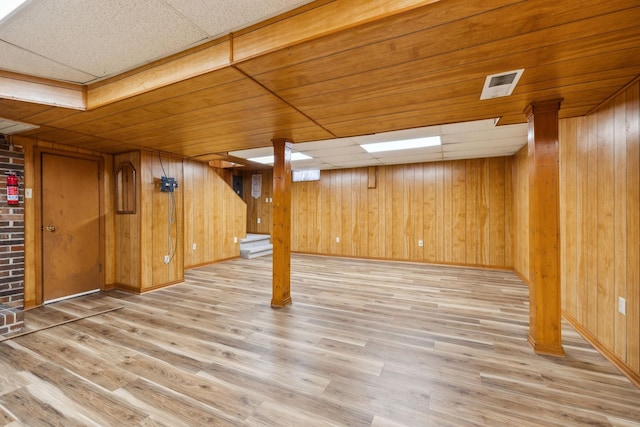 finished below grade area with a drop ceiling, wood walls, and light wood-style flooring