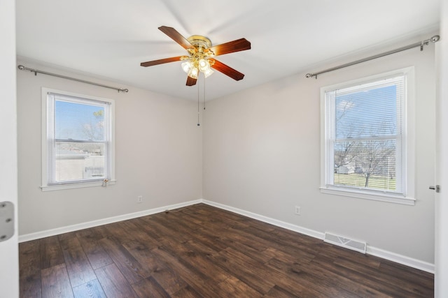 spare room with dark wood-type flooring, a healthy amount of sunlight, visible vents, and baseboards