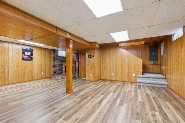 finished below grade area featuring a paneled ceiling, light wood-style flooring, wood walls, and electric panel