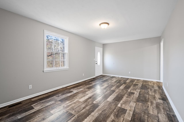 empty room with visible vents, baseboards, and dark wood finished floors