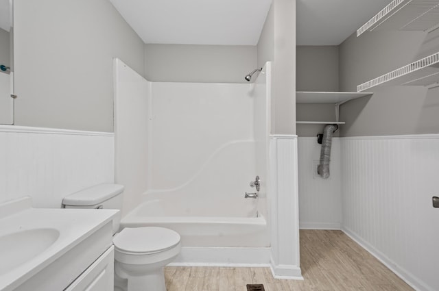 bathroom with toilet, wainscoting, vanity, shower / tub combination, and wood finished floors