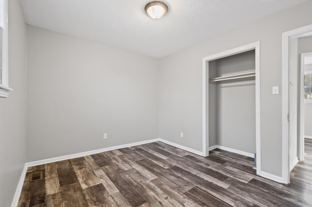 unfurnished bedroom featuring baseboards, a closet, visible vents, and dark wood-style flooring