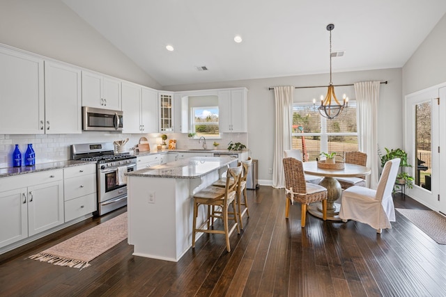 kitchen with light stone counters, stainless steel appliances, a kitchen island, white cabinetry, and glass insert cabinets