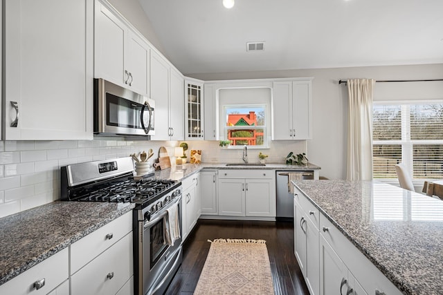 kitchen with appliances with stainless steel finishes, stone counters, glass insert cabinets, and white cabinetry