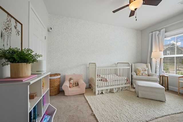 carpeted bedroom with a crib, wallpapered walls, ceiling fan, and visible vents