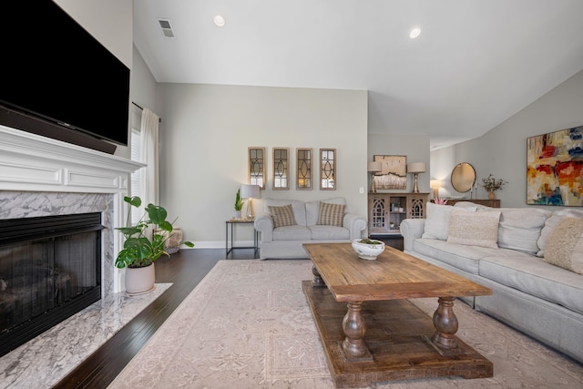 living area featuring visible vents, dark wood-type flooring, a high end fireplace, vaulted ceiling, and baseboards