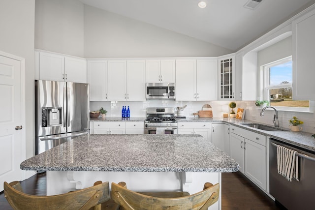 kitchen featuring stainless steel appliances, glass insert cabinets, white cabinets, a sink, and light stone countertops