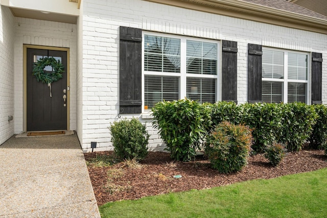 doorway to property featuring roof with shingles and brick siding