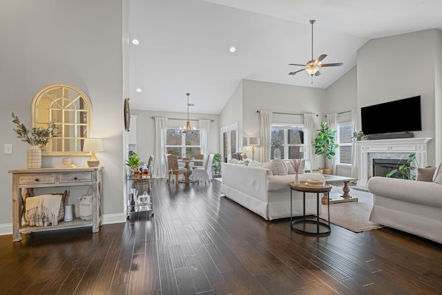 living room with dark wood-style flooring, a premium fireplace, high vaulted ceiling, baseboards, and ceiling fan with notable chandelier