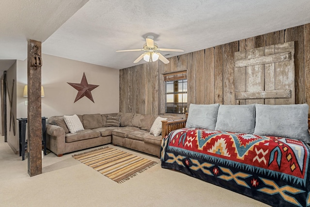 living room with wooden walls, a ceiling fan, a textured ceiling, and light colored carpet