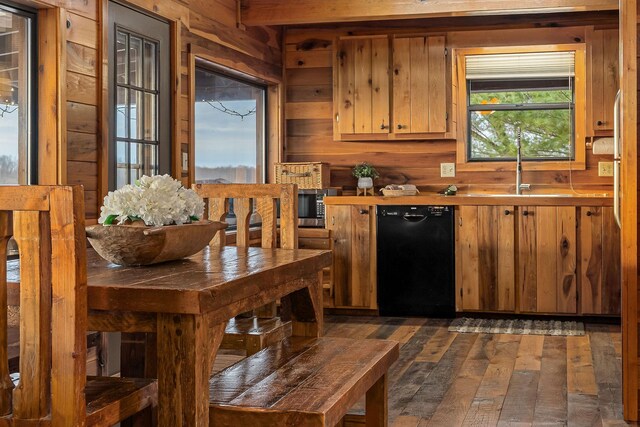 kitchen with black dishwasher, brown cabinetry, dark wood finished floors, and wooden walls