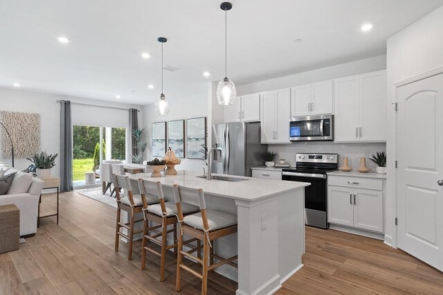 kitchen featuring a kitchen island with sink, a sink, white cabinetry, appliances with stainless steel finishes, and pendant lighting