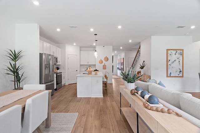 kitchen with stainless steel appliances, white cabinetry, open floor plan, light countertops, and decorative light fixtures