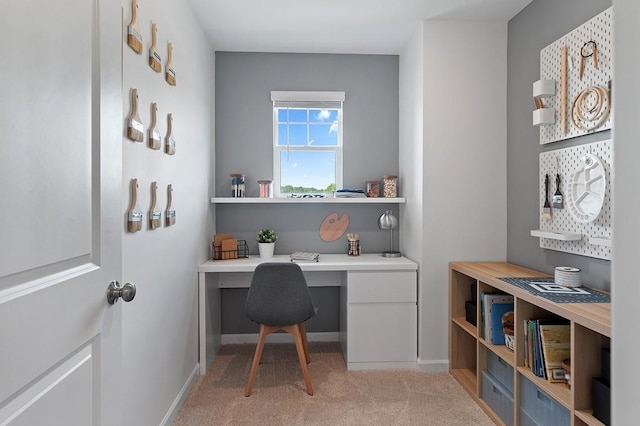 office space featuring light carpet, built in desk, and baseboards