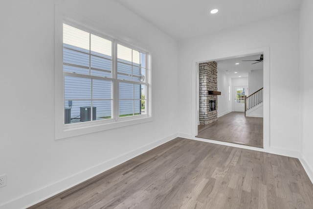 spare room featuring recessed lighting, a fireplace, baseboards, stairway, and light wood finished floors