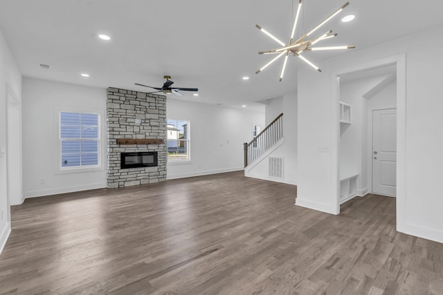 unfurnished living room with stairs, visible vents, a stone fireplace, wood finished floors, and ceiling fan with notable chandelier