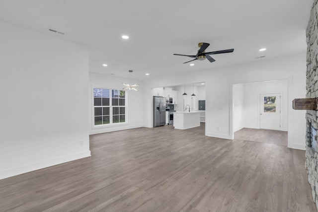 unfurnished living room with a fireplace, light wood finished floors, visible vents, a sink, and ceiling fan with notable chandelier