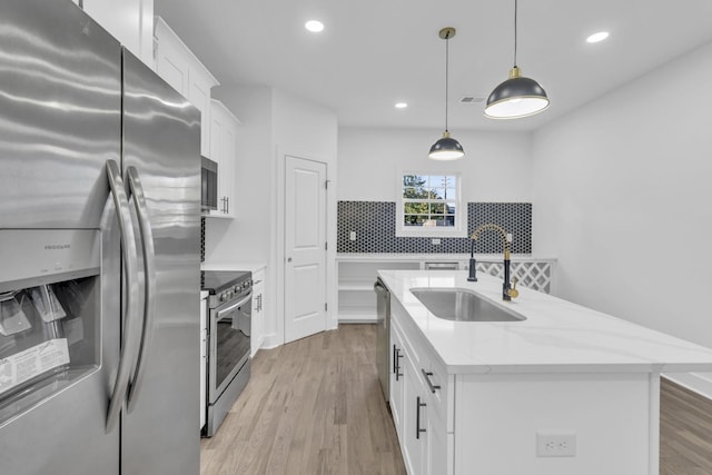 kitchen with appliances with stainless steel finishes, an island with sink, a sink, and white cabinetry